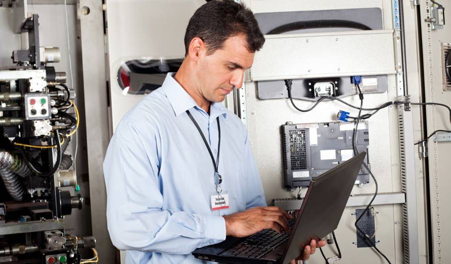 Facilities technician working on a laptop beside an electrical control panel